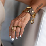 Funky two-finger ring in gold, featuring a smooth, irregular geometric design worn on two fingers with a gold bracelet.