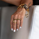 Gold two-finger ring with a fluid, geometric design, worn on a hand with white nails, showcasing an edgy style.
