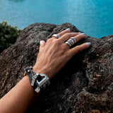 Bold snake chains bracelet with a woven leather band in shades of brown or black, showcased on a hand resting on a rock.