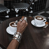 Chunky minimalist metallic cuffs in a silver finish worn on a hand holding a spoon over a coffee cup.