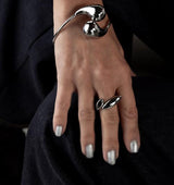 Adjustable wavy silver ring on a hand, featuring a flat wavy design, worn alongside a shiny silver bracelet.