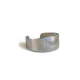 Chunky minimalist metallic cuff bracelet with a wide flat design, rhodium plated finish, and adjustable fit.