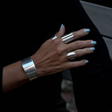Chunky metallic cuffs and rings showcased on a hand, featuring sleek silver designs with a minimalist, edgy style.
