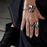 Adjustable wavy silver ring worn on a hand with silver nail polish, featuring a modern flat wavy top and a shiny finish.