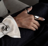 Adjustable wavy silver ring displayed on a hand with metallic polish, paired with a sleek silver cuff bracelet.