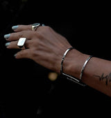 Chunky minimalist metallic cuff bangles stacked on a hand, featuring a wide flat cuff and an open double band cuff, shiny silver tone.