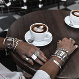 Set of chunky minimalist metallic cuffs worn stacked on a hand, showcasing a variety of silver-tone bangles and rings.