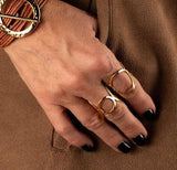 Hammered gold-plated adjustable ring with a circular geometric design, shown worn on a hand with dark nails.