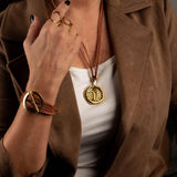 Hammered gold-plated adjustable ring with a circular geometric design, worn alongside layered necklaces and a bracelet.