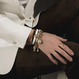 Hammered gold-plated metal ring featuring a circular geometric design, worn on the right hand with layered bracelets.
