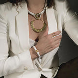 Hammered gold-plated adjustable ring featuring a circular geometric design, worn alongside a bold necklace.