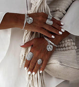 Set of four bohemian silver rings featuring floral and ethnic designs, worn on hands with white nails and a textured background.