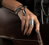 Set of four boho rings worn on a hand resting on a brown chair. Features a large oval ethnic calendar ring with intricate designs.