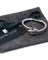 Silver-plated stackable bangle bracelet with a unique design, resting on a suede gift pouch beside a brand tag.