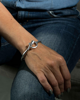 Silver-plated stackable cuff bracelet featuring a unique clasp, worn on a wrist, paired with casual denim attire.