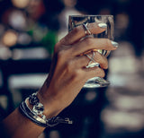Silver Edgy Punk Rings Set worn on fingers, featuring minimalist designs. Hand holding a glass, with polished nails and stacked rings.