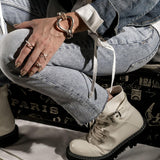 Five silver-tone punk rings worn on a hand resting on a knee, paired with light-blue denim and white chunky boots.