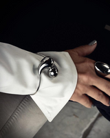 Elegant cuff bracelet in polished stainless steel with large drops, worn over a white sleeve on the wrist.