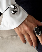 Elegant stainless steel cuff bracelet with large polished drops worn over a white shirt sleeve, showcasing a modern design.