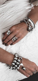 Silver-tone shell pearl bracelet featuring a thick silver-plated brass chain, worn alongside chunky rings and bracelets.