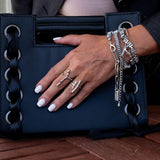 Adjustable funky bar rings worn on a hand with silver and white nail polish, against a black handbag backdrop.