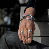 Adjustable double silver rings connected by a chain with horse bit, worn on a hand resting on a knee.