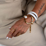 White leather triple wrap bracelet featuring a hammered gold loop and stainless steel chain; worn on a wrist with gold rings.