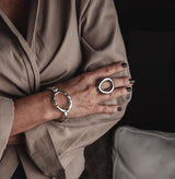 Chunky stainless steel ring worn on a finger, paired with a matching bracelet, both featuring a sleek, modern design.