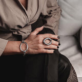 Chunky stainless steel ring with a circular design, worn on the hand, paired with a matching bracelet.