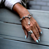 Chunky stainless-steel rolo chain bracelet features a shackle, teardrop pendant, and grey crystal, styled on a hand.