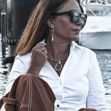 Chunky teardrop charm hoop earrings with sterling silver finish, worn casually with a white shirt and layered necklace.