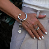 Bold arrow bracelet in silver-plated Zamak with soft brown leather, worn on the wrist alongside a chunky ring.