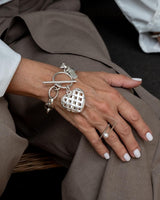 Textured heart charm bracelet in antique-plated 999 silver, worn on a wrist with a casual silver ring and white nails.