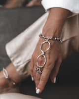 Handmade stainless steel hand harness featuring a ring connected to a bracelet with bold, fluid links draping over the hand.