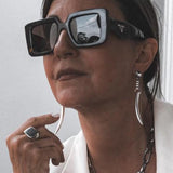 Long silver tiger's tooth spike earrings dangle from the model's ears, paired with a chunky silver ring and oversized sunglasses.