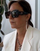 Long tiger's tooth spike earrings in silver, worn by a model with dark hair, paired with a chunky chain necklace and sunglasses.