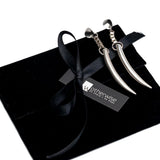 Long, silver-plated tiger's tooth spike earrings displayed on a black suede pouch, featuring a shiny, edgy design.