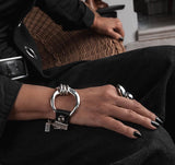 Edgy silver large hoop bracelet features a chunky cuff design with a genuine black leather strap and a horse bit detail.