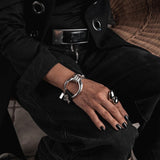 Chunky silver large hoop bracelet with a black leather band, worn on a model's wrist. Features a unique horse bit design.