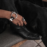 Chunky silver hoop and leather bracelet worn on a hand, paired with a black leather boot; features a brutalist design.