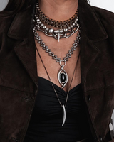 Layered gold and silver chokers and necklaces with varied textures, featuring a prominent black oval pendant.