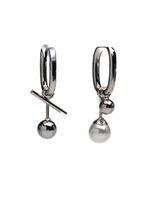 A pair of silver huggie hoop earrings, one shown from the front with a diagonal bar detail and a dangling ball, and the other from the side showing a small bead and a larger pearl-like drop, set against a plain white background.