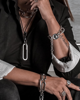 Person wearing multiple silver chain bracelets and a necklace indoors.