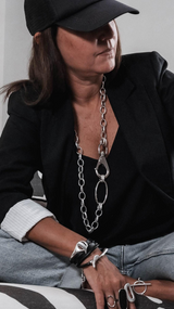 Person wearing a black cap and black jacket with silver jewelry, sitting on a zebra-patterned chair.