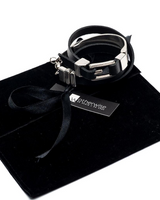 Black leather bracelet with silver accents on a black velvet surface, branded 'otherwise'.