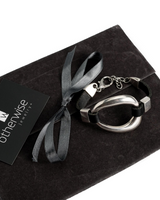 Adjustable black leather and silver metal cuff bracelet with a unique design, presented on a black suede pouch.