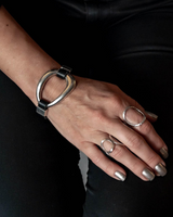 Black leather and silver metal cuff bracelet worn on a model's wrist, paired with silver rings and dark attire.