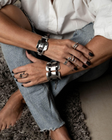 Close-up of a person's hands with multiple bracelets and rings on a textured surface.