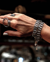 Layered stainless steel cuff and chain bracelets stacked on a wrist, showcasing an oversized loop buckle and pendant detail.