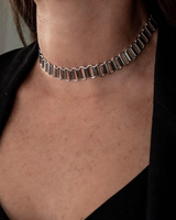 Silver choker necklace worn by a person against a neutral background